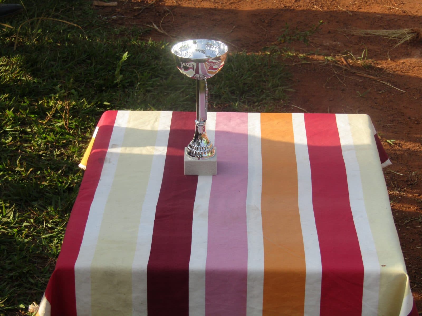 Une coupe posée seule sur une table nappée, au bord d'un terrain de terre.